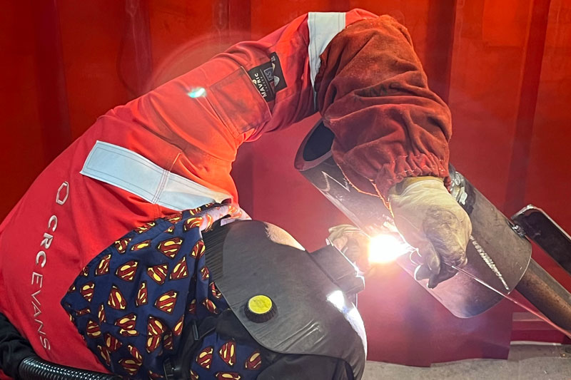 person in a CRC Evans branded overall, a bandana and helmet welds an exhaust