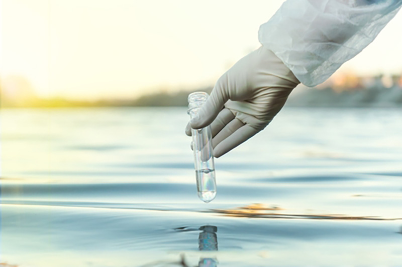 gloved hand holding a part filled test tube by a body of water