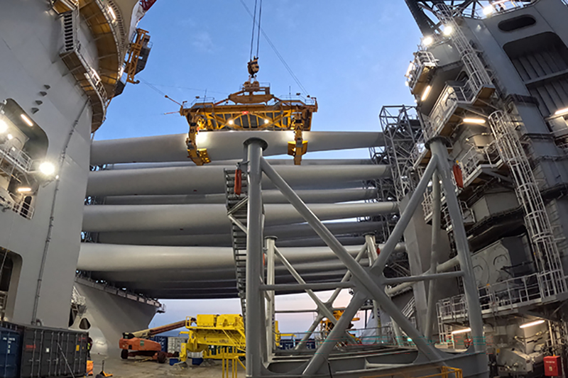 Looking up at stacked-up wind turbine blades being unloaded by a boat crane